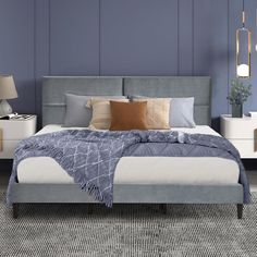 a bed with blue sheets and pillows in a room next to two lamps on either side of the bed