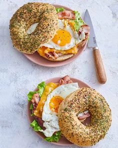 two plates with bagels and an egg sandwich on them, next to a knife