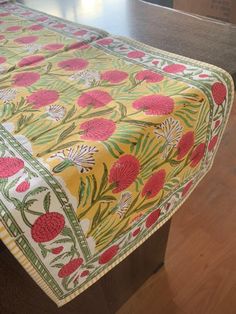 a table with a yellow and red flowered tablecloth on it, sitting on a wooden surface