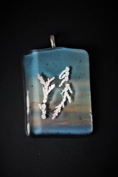 a square glass pendant with white flowers on the front and back of it, hanging from a black background