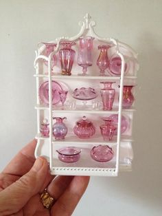 a hand holding a small shelf with pink glass items on it's sides,