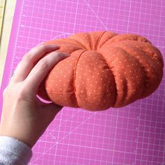 someone is holding a pumpkin shaped pillow on a cutting board