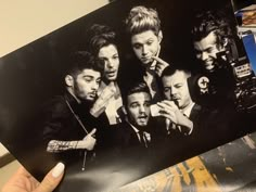 a hand holding up a black and white photo of the backs of one direction band members