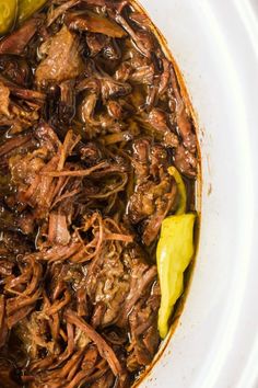 a white bowl filled with shredded meat and pickles on top of a wooden table