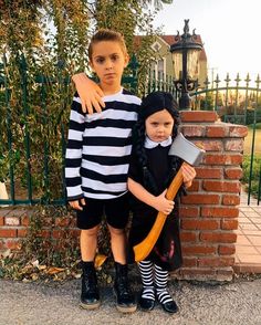 two children dressed in costumes standing next to each other near a brick wall and fence