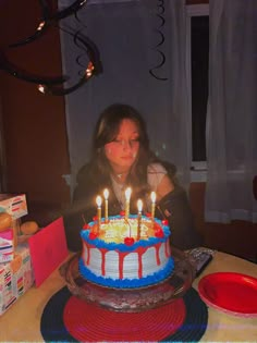 a woman sitting in front of a birthday cake with lit candles on top of it