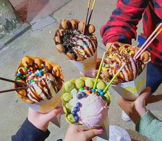 four people holding ice cream sundaes with sprinkles and toppings