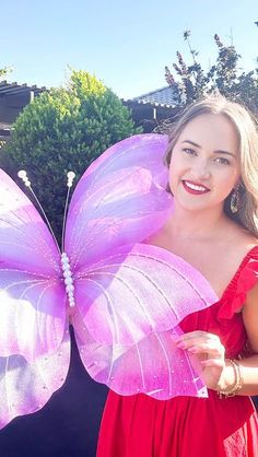 a woman in a red dress is holding a pink butterfly shaped object and smiling at the camera