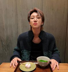 a woman sitting at a wooden table with a bowl of soup and an egg on the plate