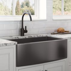 a stainless steel sink in a kitchen with marble counter tops and white cabinets, along with two windows