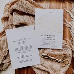 the wedding stationery is laid out on top of a piece of fabric and some gold scissors