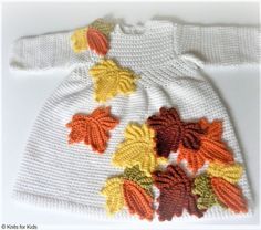 a white knitted sweater with leaves on the front and bottom, sitting on top of a table