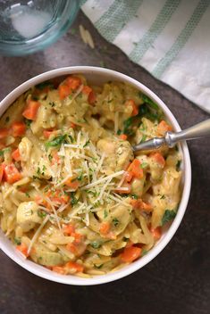 a bowl of pasta with carrots and parmesan cheese in it next to a glass of water