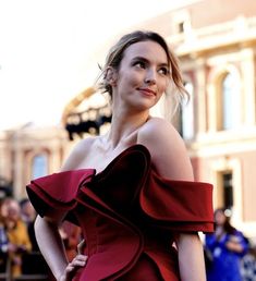 a woman in a red dress posing for a photo on the street with people behind her