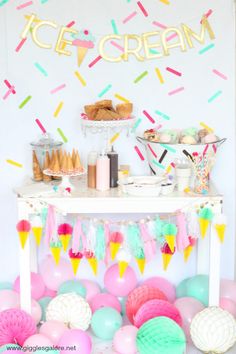 an ice cream stand with lots of balloons and confetti on the table in front of it