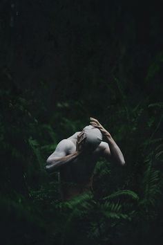 a woman with her hands on her head standing in the middle of green plants and ferns