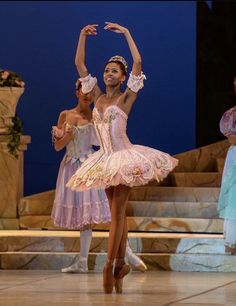 two ballerinas in tutu and leotards on stage with one holding her arm up