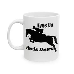 a white coffee mug with an image of a horse and rider that says eyes up heels down