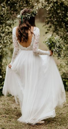 a woman in a white dress is walking through the woods with her back to the camera