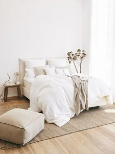 a white bed sitting on top of a wooden floor next to a chair and ottoman