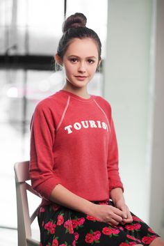 a young woman sitting on top of a chair wearing a red shirt and floral skirt