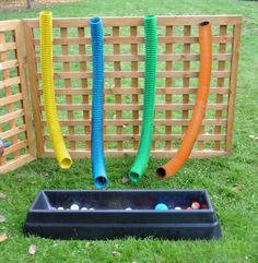 an outdoor play area with plastic pipes and balls in the ground, near a wooden fence