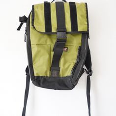 a green and black backpack sitting on top of a white wall