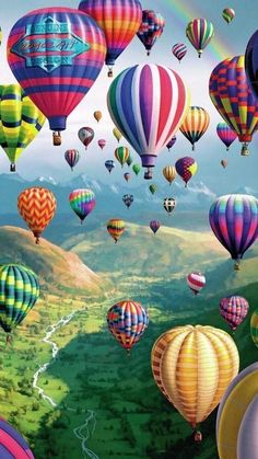 many colorful hot air balloons flying in the sky over a valley and mountains with a rainbow