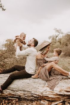 a man holding a baby while sitting on top of a log with two other people