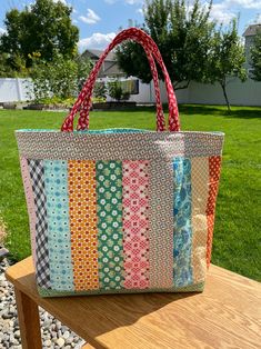 a multicolored bag sitting on top of a wooden bench in front of some grass