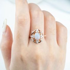 a woman's hand holding a ring with a white opal and diamond center