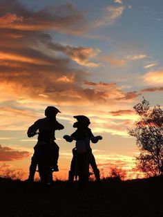 two people standing on top of a hill near the sky at sunset with clouds in the background