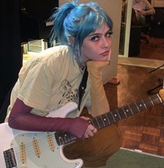 a woman with blue hair is holding a guitar and posing for the camera in front of her