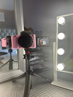 a pink camera sitting on top of a tripod in front of a large mirror