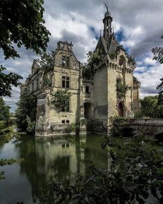 an old castle sitting on top of a river next to a lush green forest under a cloudy sky