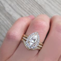 a person's hand holding a ring with two gold bands and a pear shaped diamond