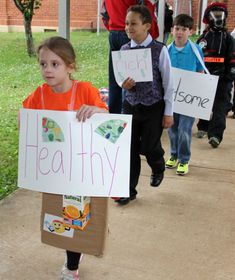 young children holding signs that read healthy and nourishment on the side walk