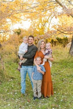 a family posing for a photo in an autumn field with leaves on the ground and trees behind them