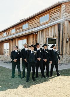 a group of men standing next to each other in front of a wooden building on grass