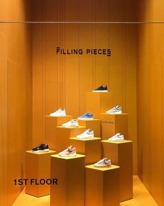 a display case filled with different types of shoes on yellow pedestals in front of a wooden wall