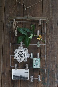 a metal rack holding pictures and flowers on a wooden wall with clothes pins, scissors and other items