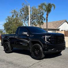 the black truck is parked on the street in front of some palm trees and houses