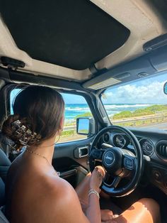 the woman is driving her car on the road by the beach and ocean in the distance