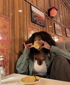 a woman sitting at a table drinking from a cup