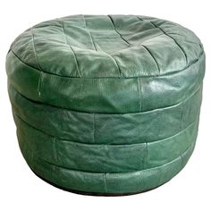 a round green leather ottoman sitting on top of a white floor next to a wall