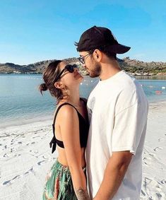 a man and woman are standing on the beach with their eyes close to each other