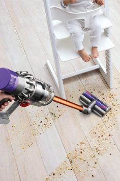 a baby is sitting in a high chair with a cordless vacuum