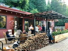 people are gathered around the firewood in front of a red building with lots of wood stacked on it