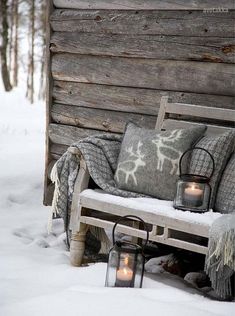 a bench with candles and blankets on it in the snow next to a log cabin