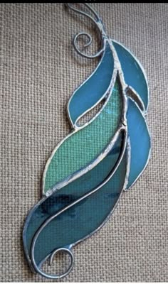 a blue and green stained glass piece hanging from a hook on a tan fabric background